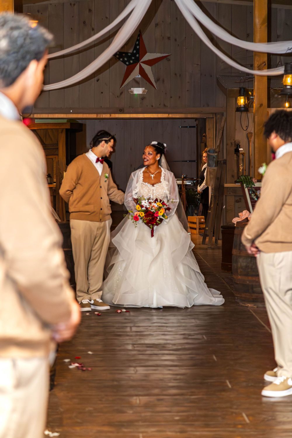 Wedding guests in beige attire form a line on a rustic wooden dance floor during a reception celebration.