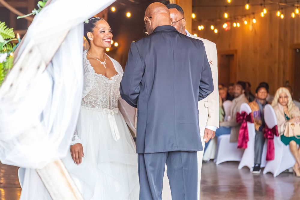 A bride and groom share their first dance at a rustic barn wedding reception with warm lighting and guests watching.
