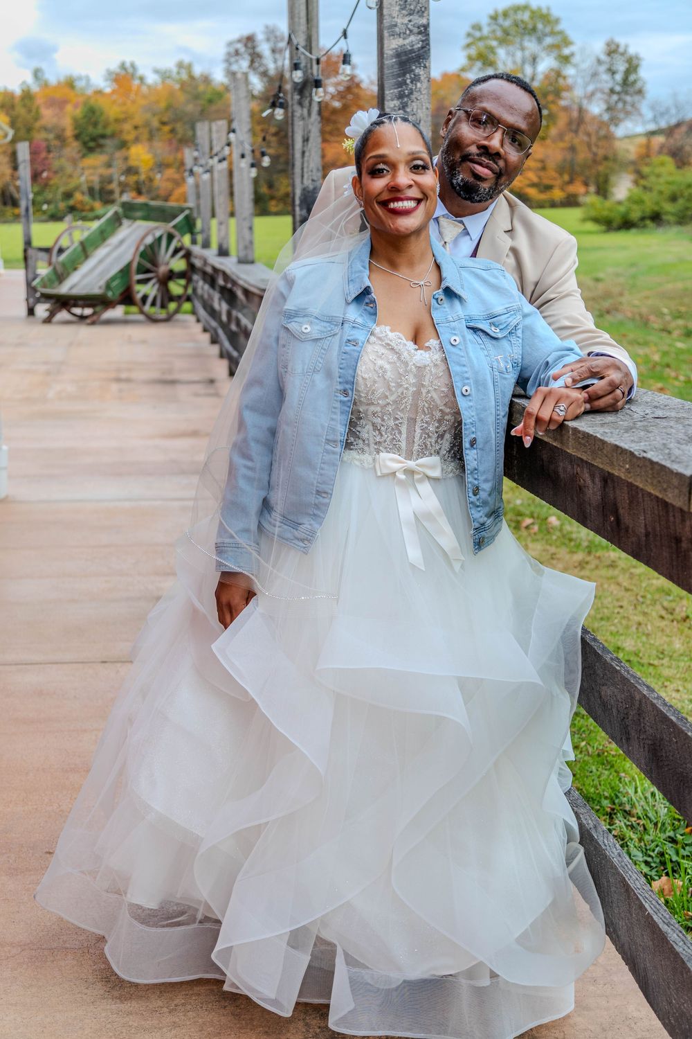 A couple shares a romantic moment in autumn, with the bride wearing a flowing white dress and denim jacket.
