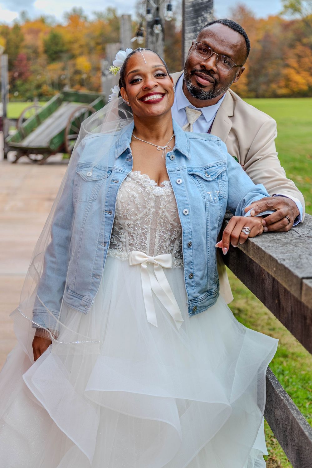 A couple poses together outdoors during autumn with fall foliage in the background.