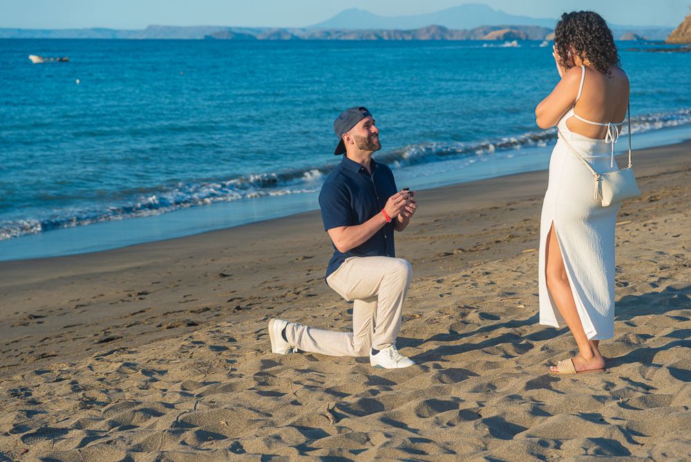 A couple poses together on a sandy beach with turquoise ocean waves rolling in behind them.
