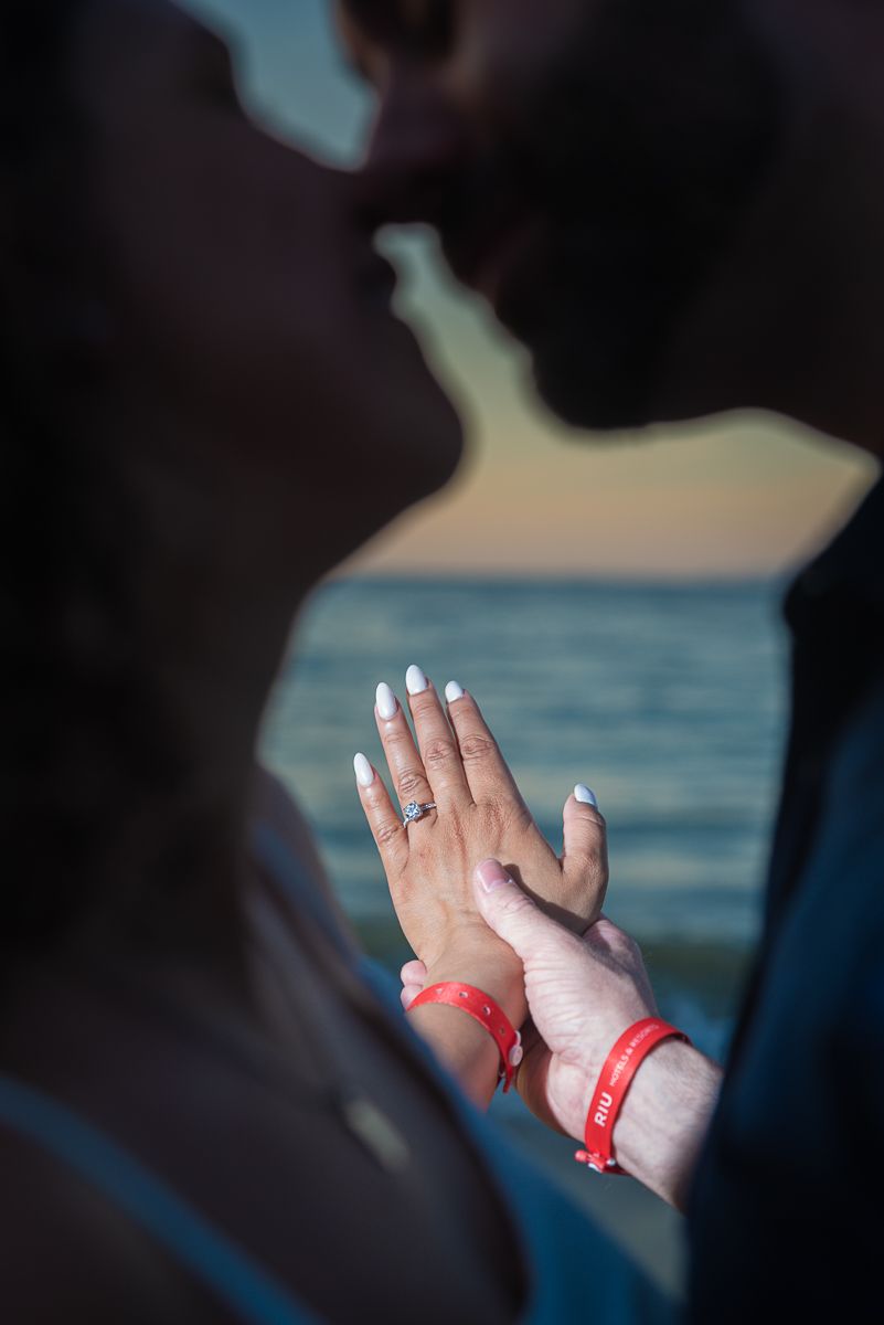 Close-up of hands showing an engagement ring against an ocean backdrop during golden hour.