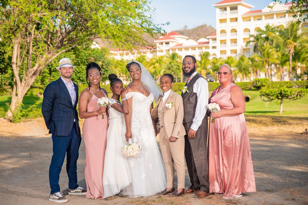 Wedding photoshoot un Riu party in pink and navy attire poses for formal photos on resort grounds.