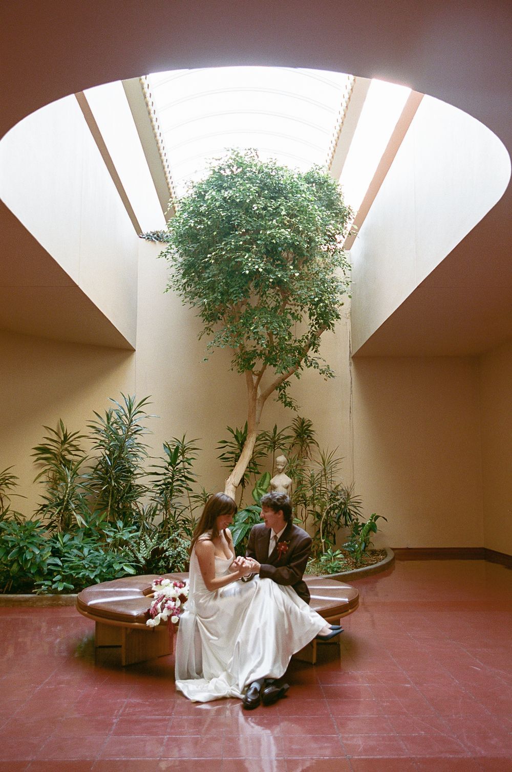 Wedding ceremony in a minimalist indoor space with natural light from skylight and potted plants.