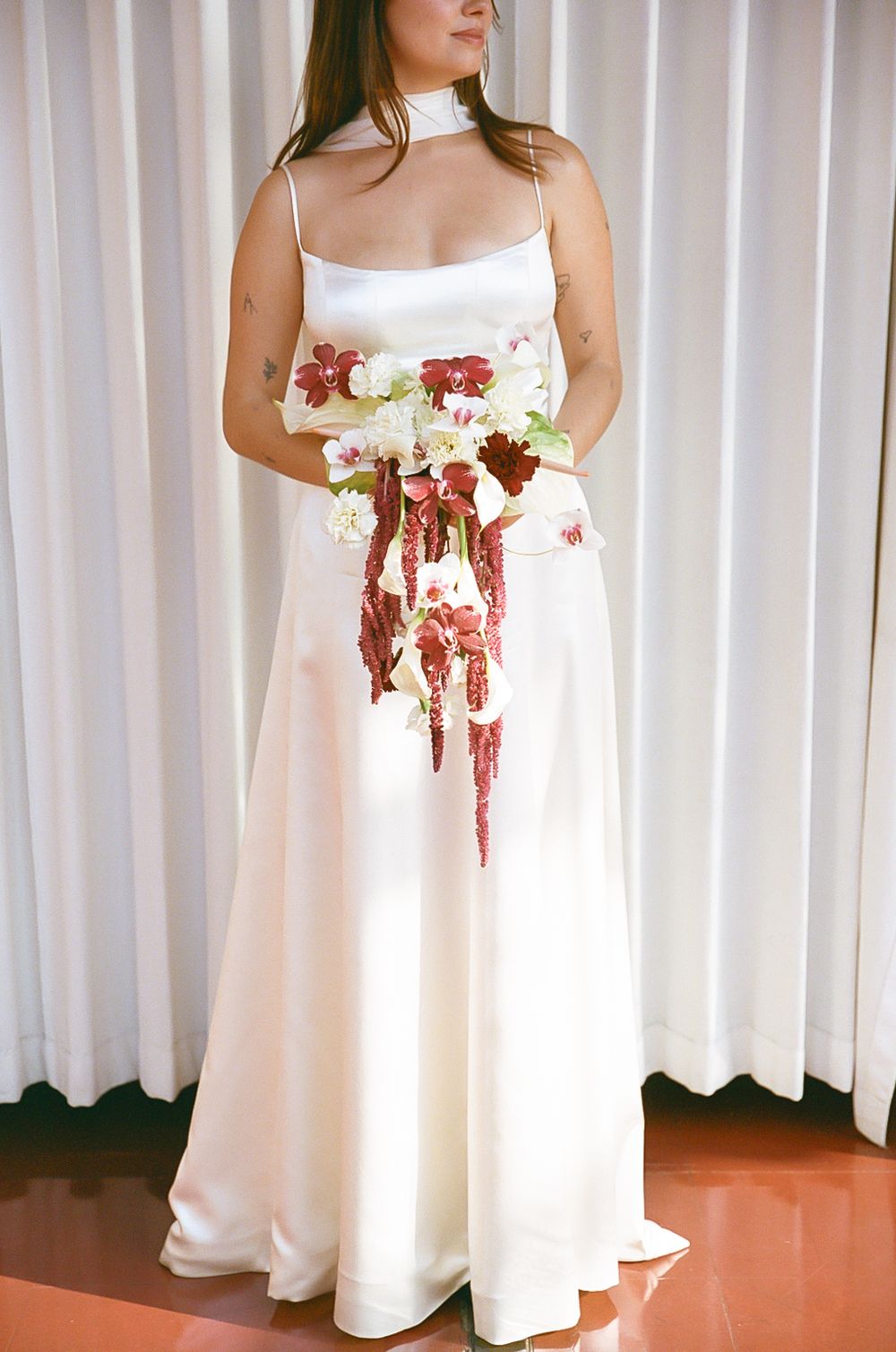Close-up details of white wedding dresses with floral accents against light curtain backdrop.