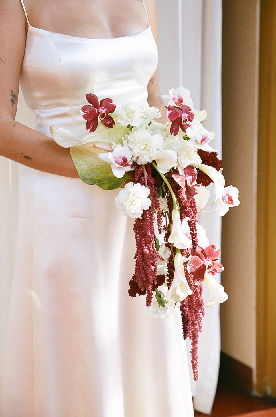 A cascading bridal bouquet featuring white and burgundy flowers with orchids against a white wedding dress.