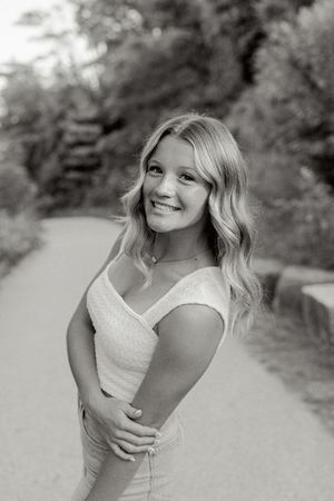 Black and white portrait on a garden path showing a bright smile and wavy blonde hair.