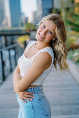 Casual summer portrait against urban backdrop featuring white crop top and high-waisted jeans.