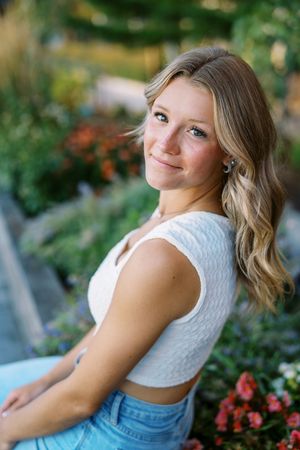 Outdoor portrait with floral garden background and white textured top.