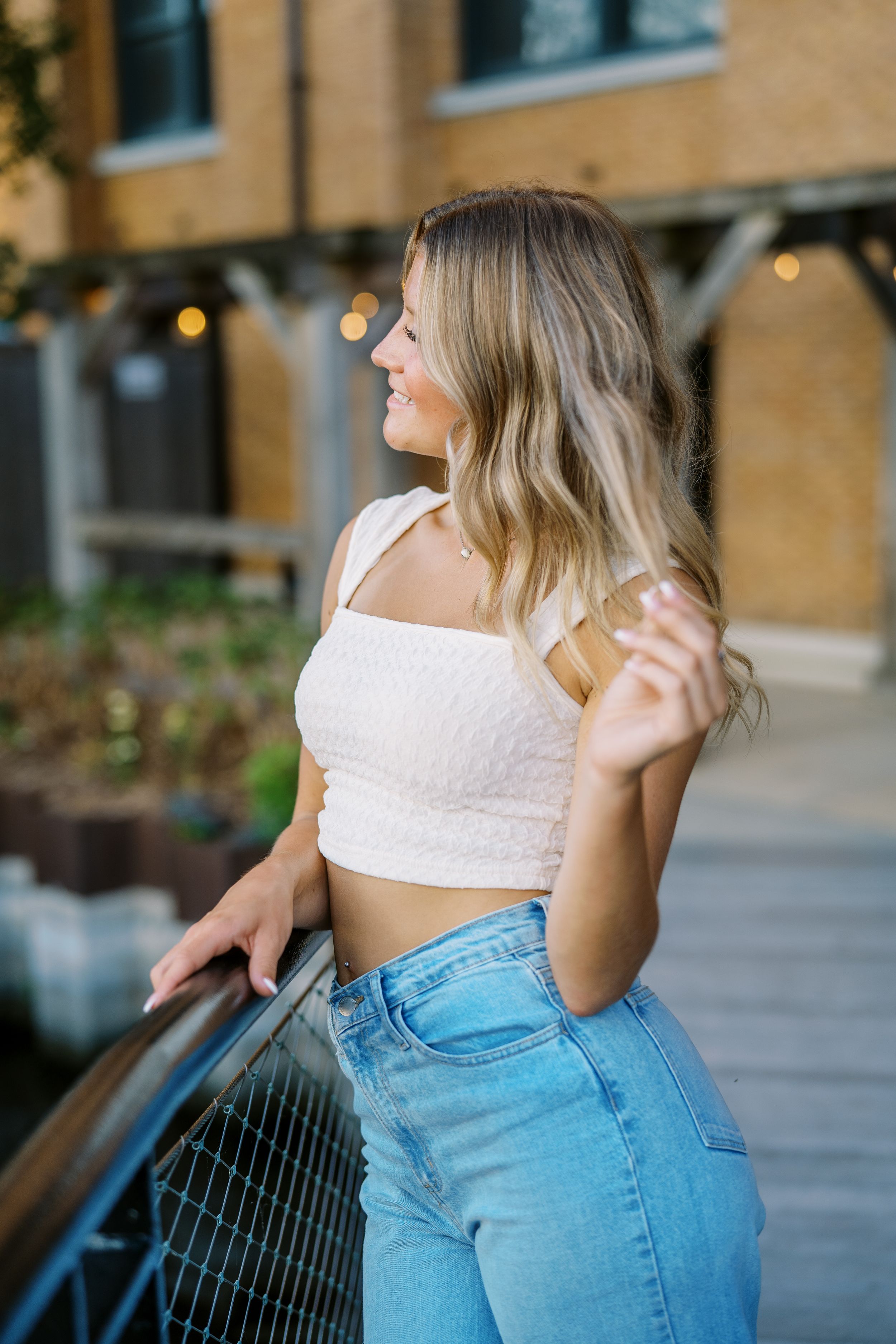 Side profile pose on urban balcony wearing white crop top and light denim.