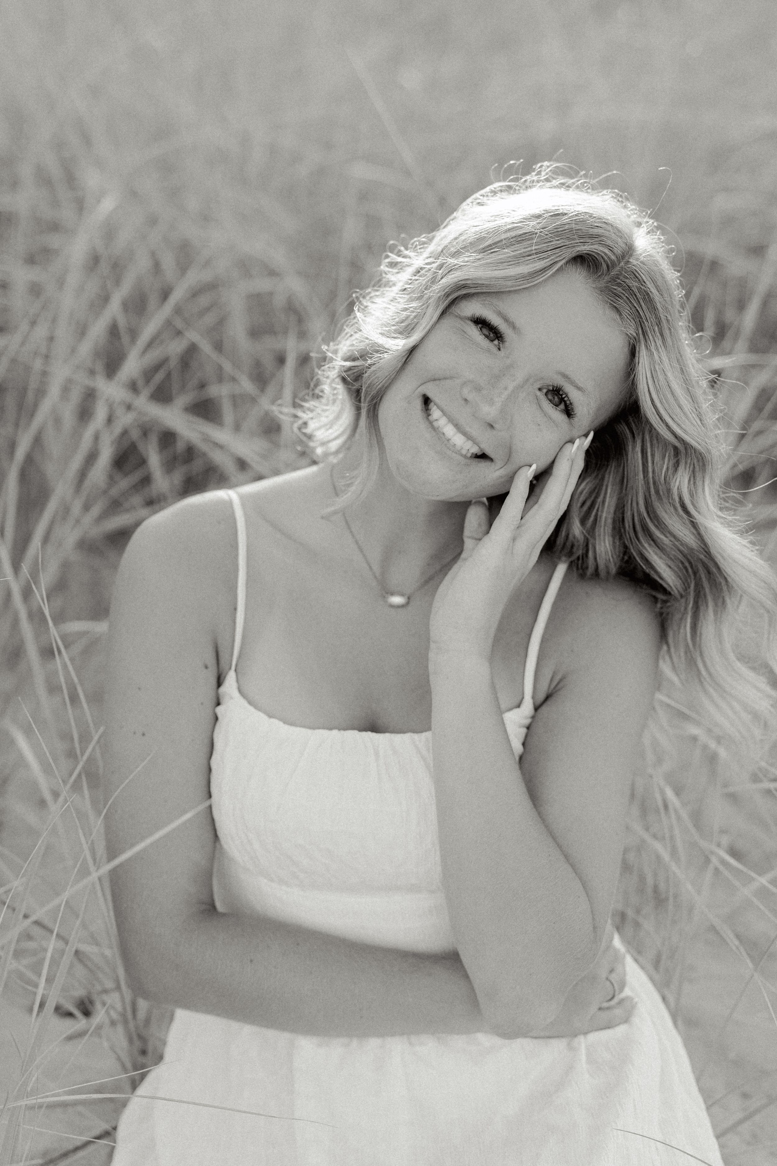 Black and white close-up portrait showing a genuine smile while touching face gently.