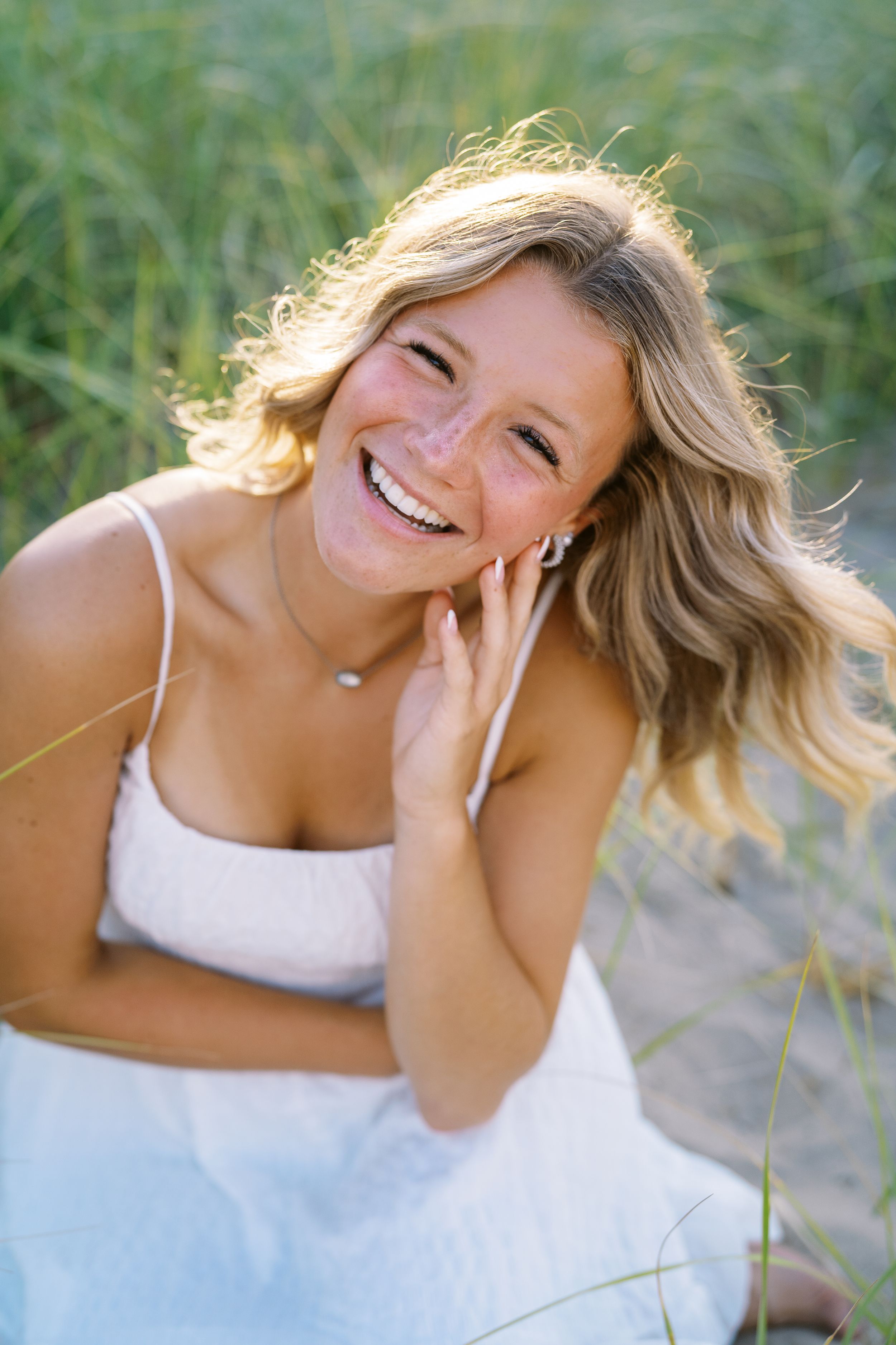 Candid laughing portrait in white dress surrounded by sunlit summer grasses.