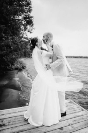 A romantic black and white photo sequence of a couple in wedding attire sharing intimate moments on a wooden dock by the water.