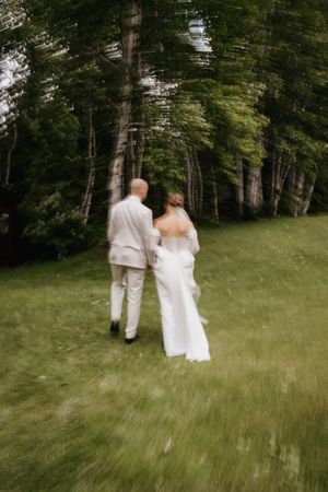 A couple in wedding attire walks hand in hand through a lush green forest clearing on their special day.
