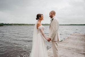 A newlywed couple shares an intimate moment on a wooden pier overlooking a lake on their wedding day.