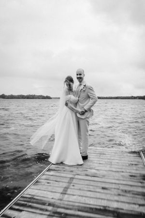 Black and white sequence of a couple on a wooden dock by a lake sharing a playful moment in wedding attire.