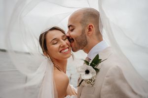 A romantic wedding moment captured under flowing white veil with an anemone and greenery boutonniere.
