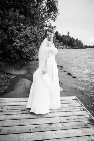 A black and white photo series showing a person in a flowing white dress standing on a wooden dock by a lake.