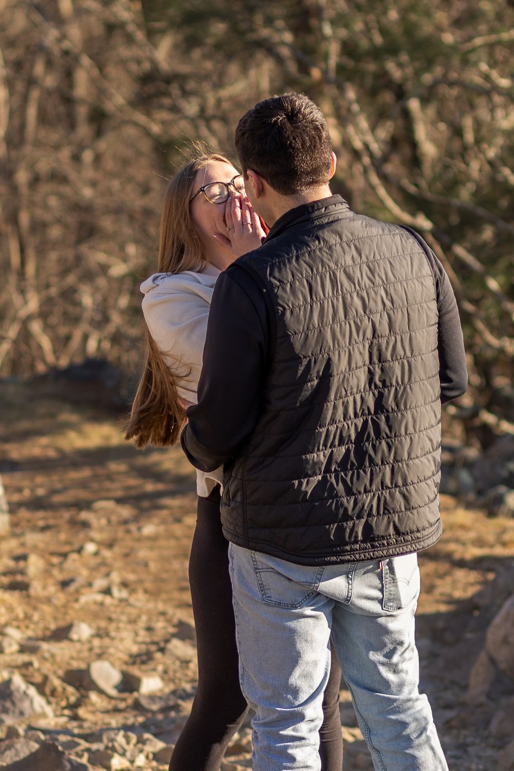 A couple embraces outdoors in a romantic moment against a natural backdrop with autumn foliage.