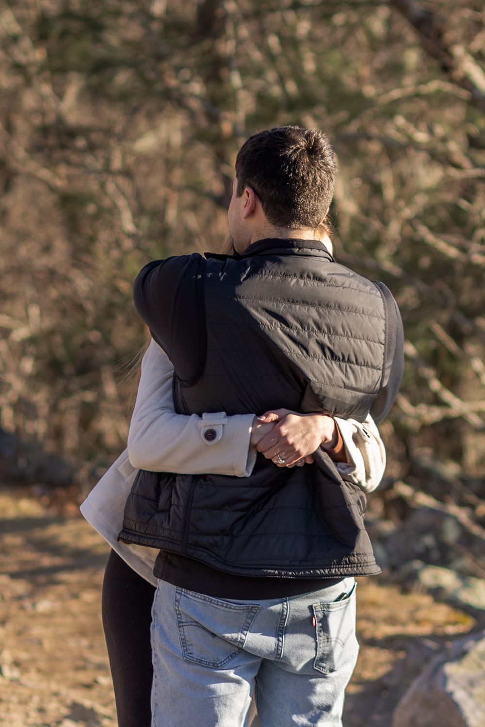 Two people share an intimate embrace outdoors against a blurred natural background during golden hour.