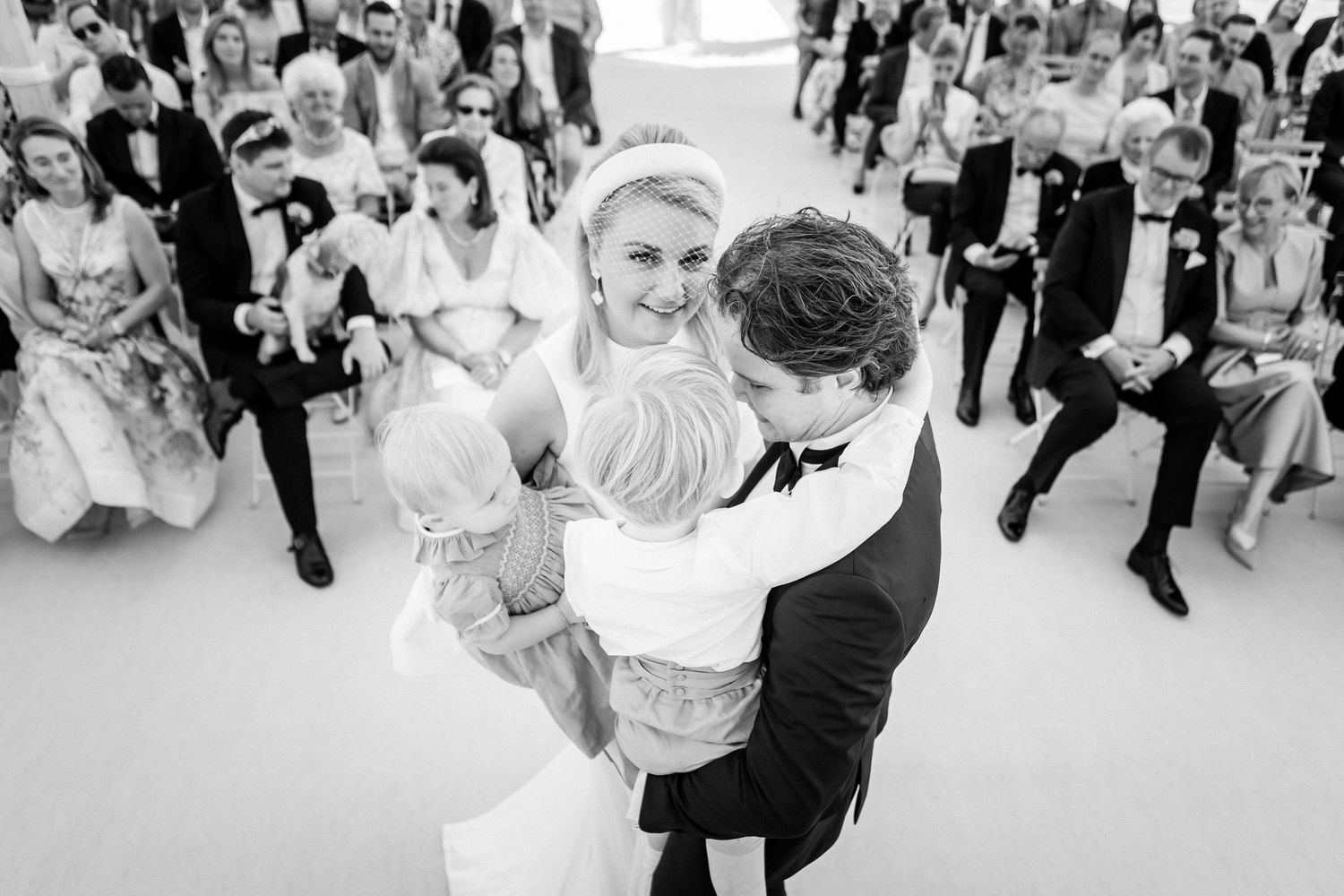 A couple shares their first dance at a wedding reception while guests watch from the dance floor in black and white.