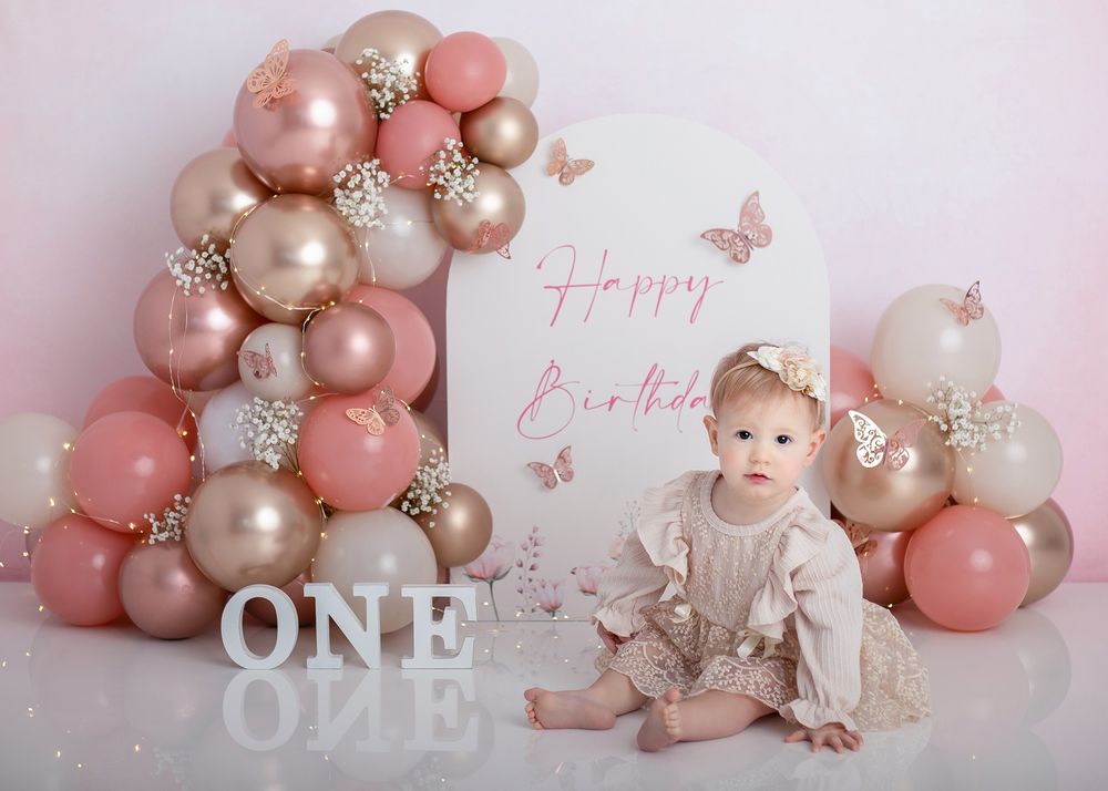 Pink and gold balloon arch decorates a first birthday party setup with elegant pastel decor and soft lighting.