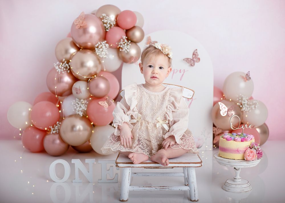 Pink and white balloon arch with pearls and floral decorations creates an elegant first birthday party backdrop.