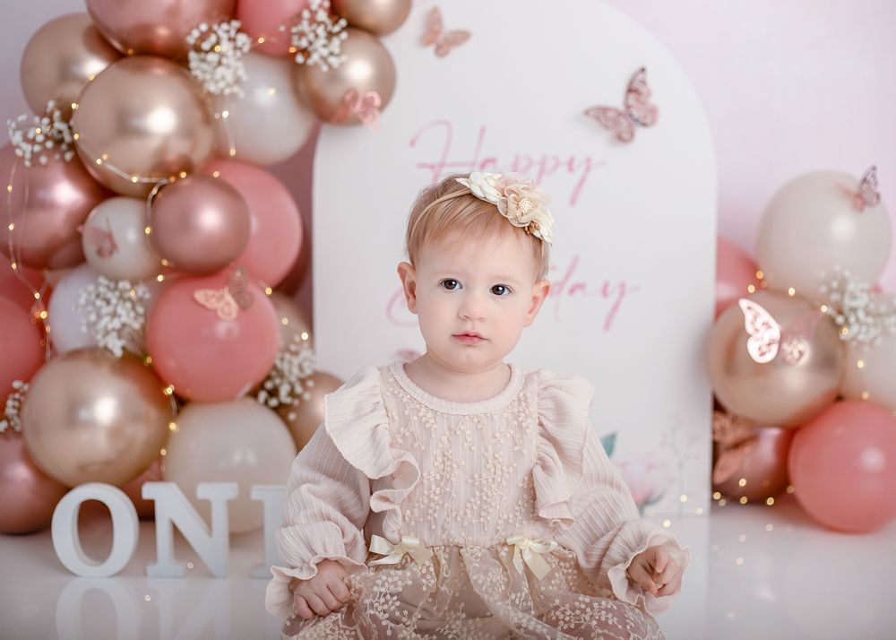 Baby's first birthday celebration setup with pink and gold balloons, butterflies, and delicate floral decorations.