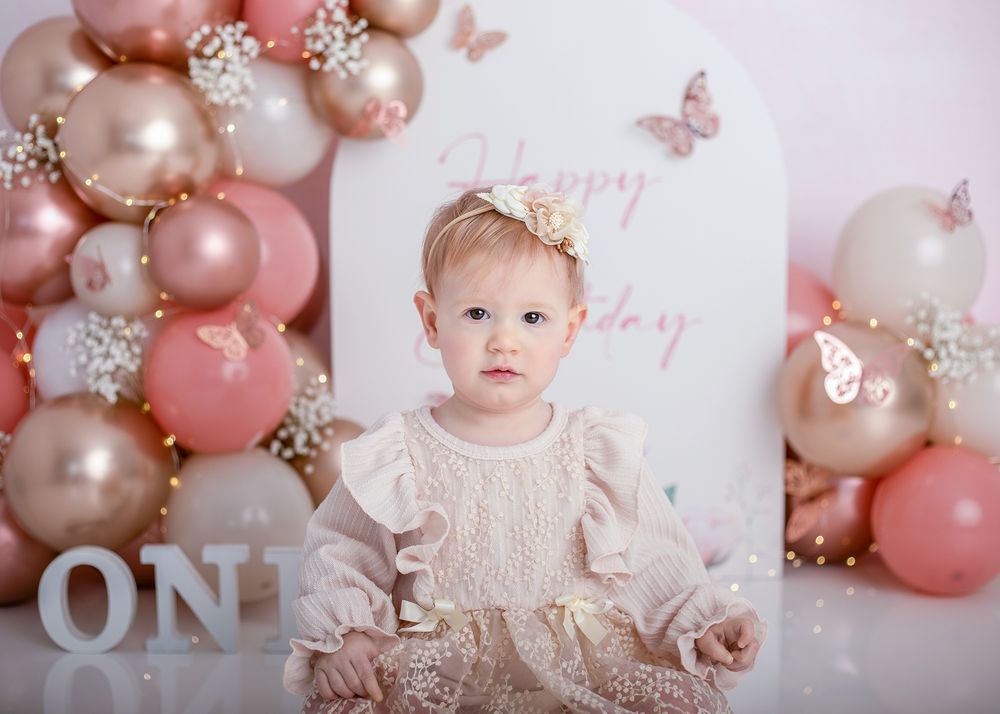Pink and gold balloon garland with butterflies and floral decorations creates a romantic first birthday party setup.
