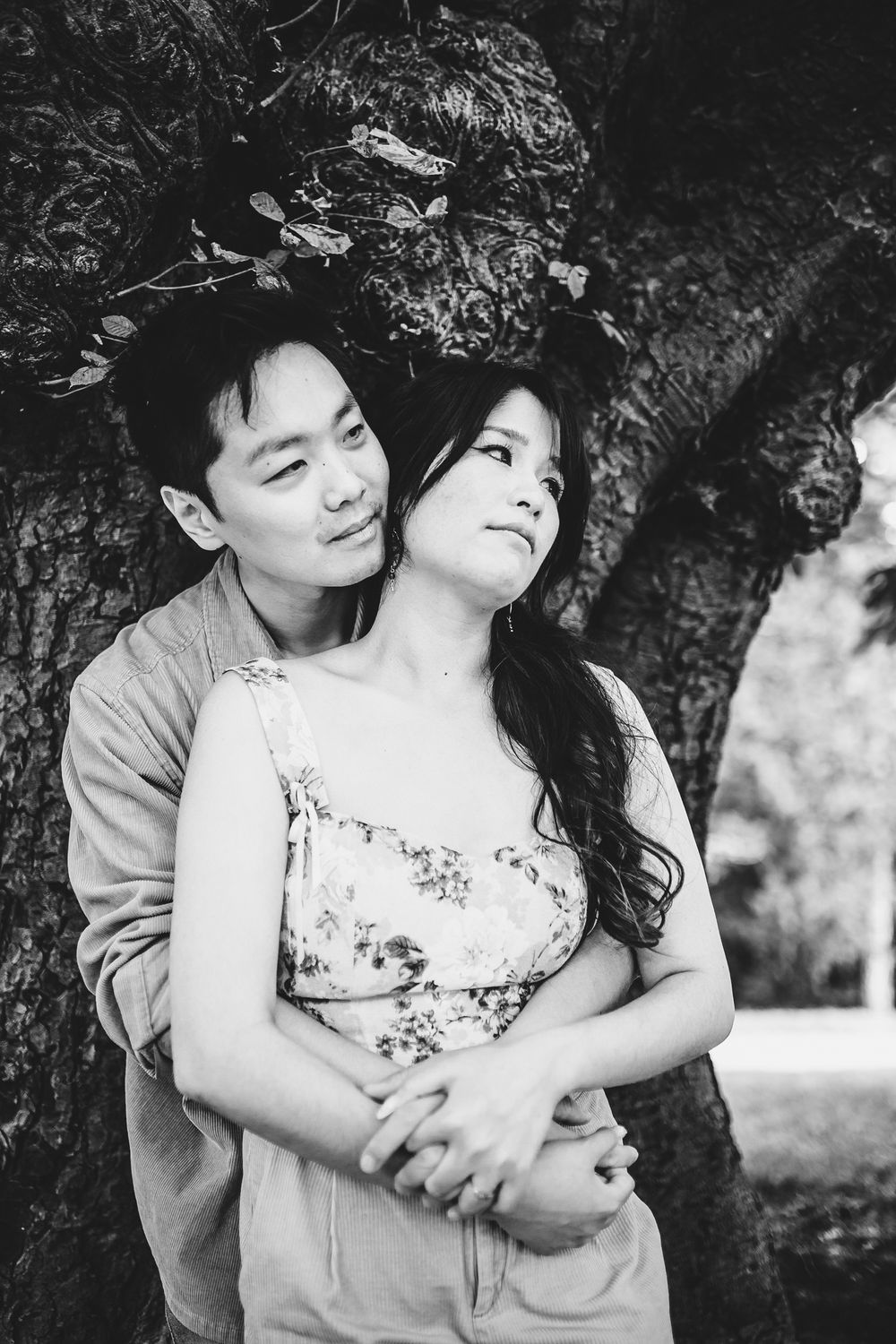 Black and white portrait of couple embracing under tree branches.