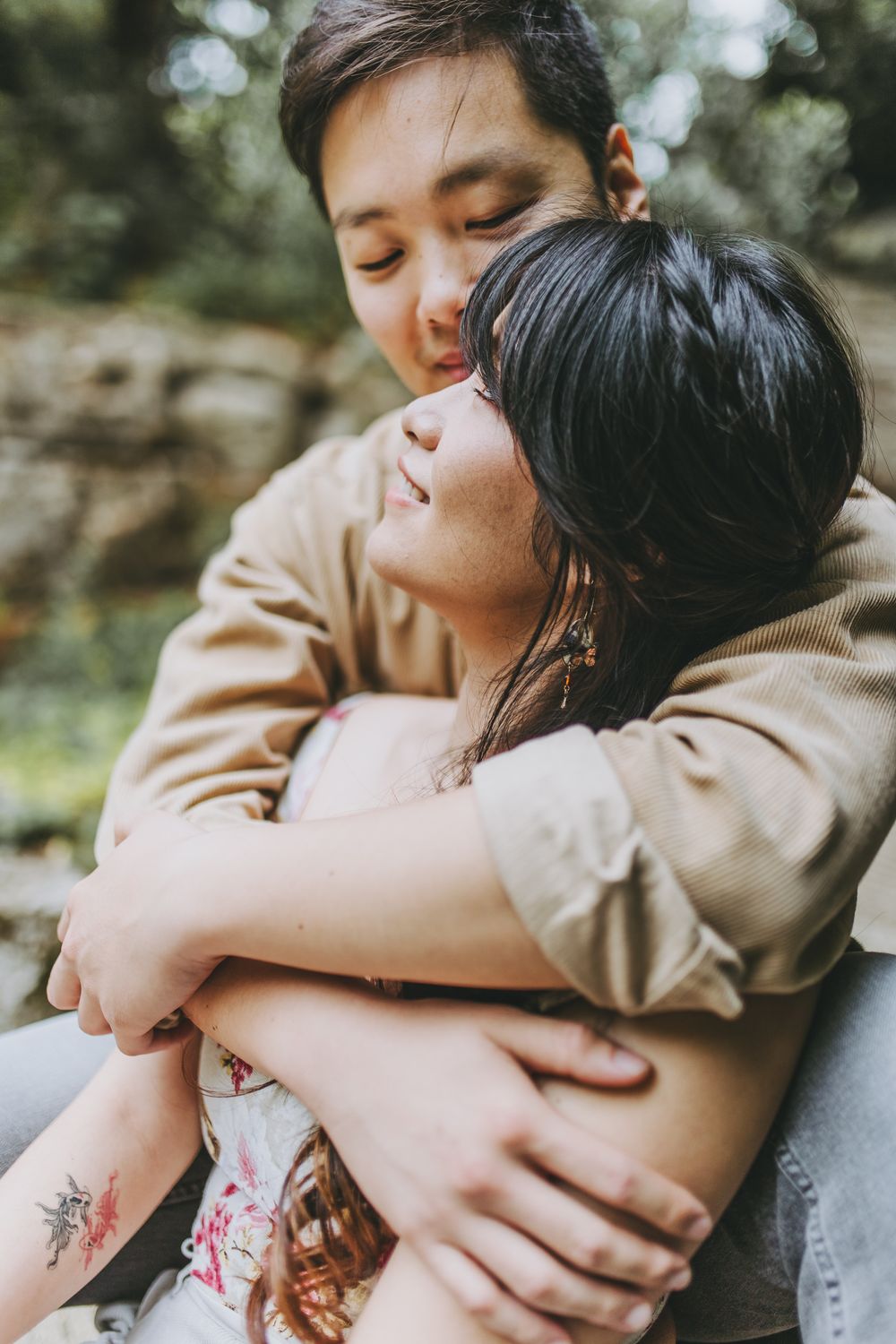 A romantic couple embraces tenderly outdoors in a natural setting with soft lighting and bokeh background.