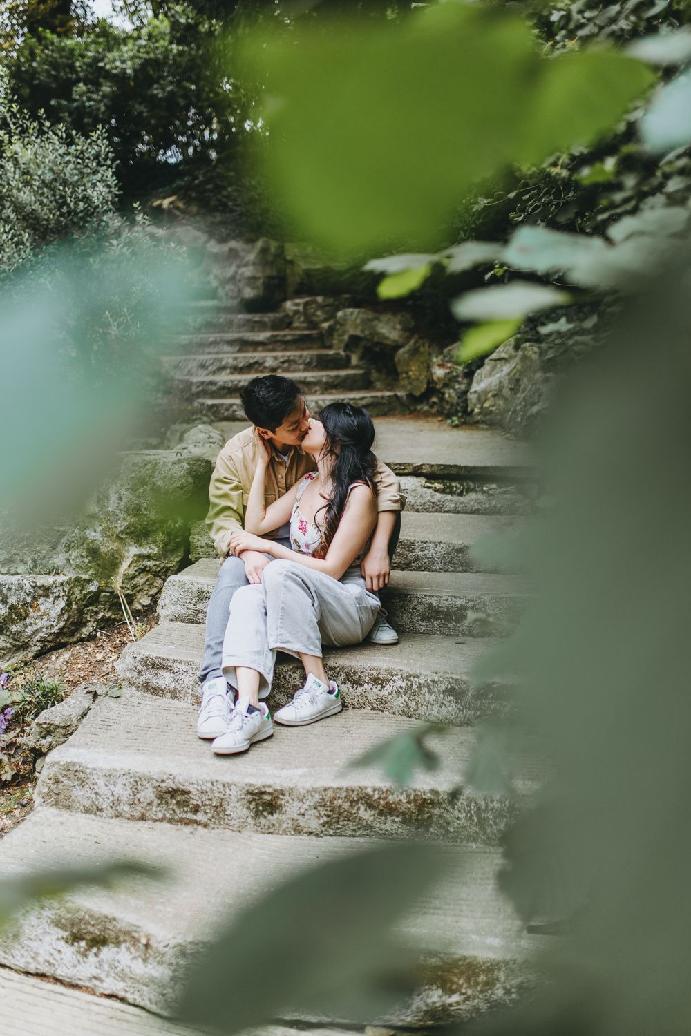 A romantic moment shared on stone steps framed by blurred green foliage.