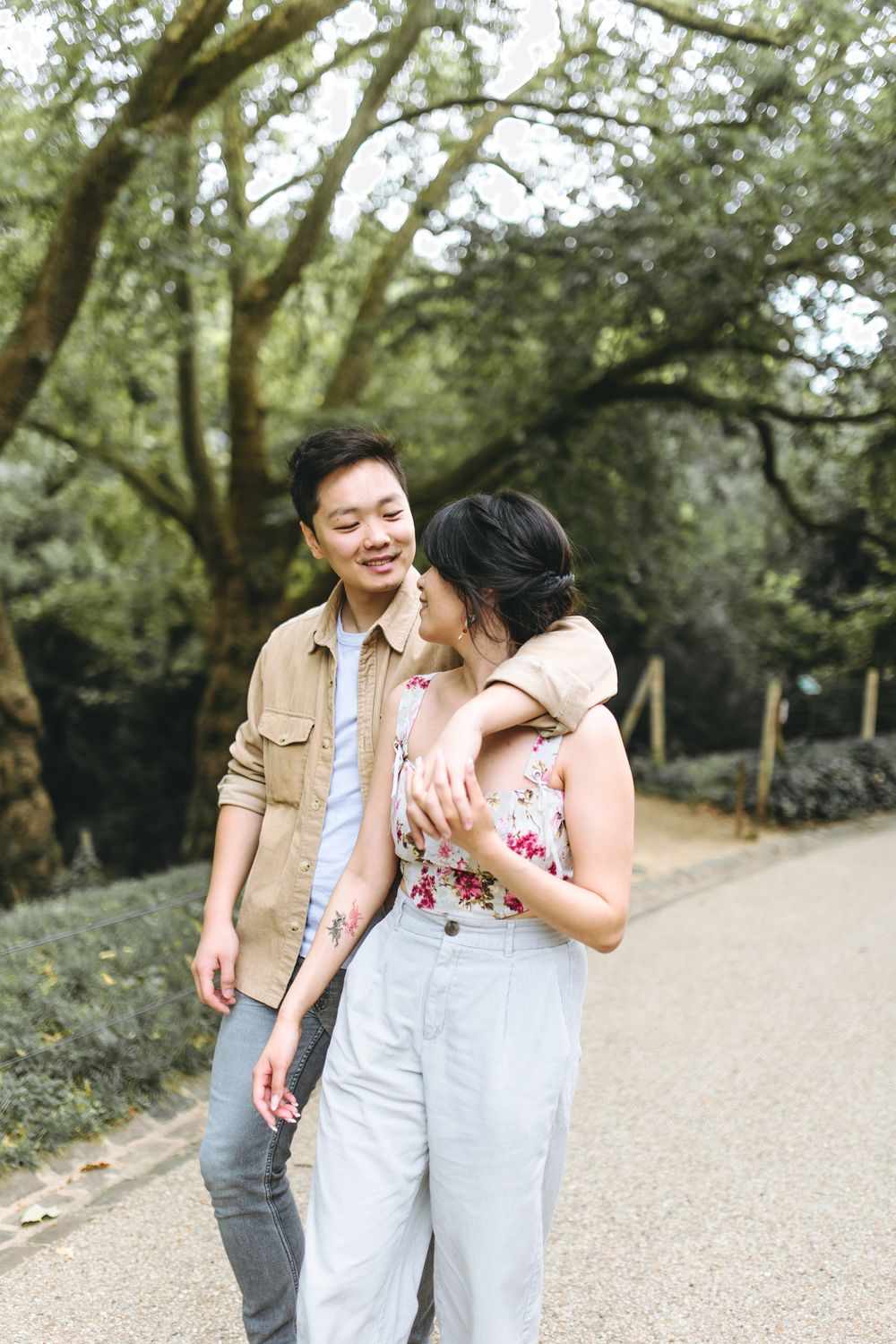 A couple shares a romantic moment while walking together on a tree-lined path in a park.