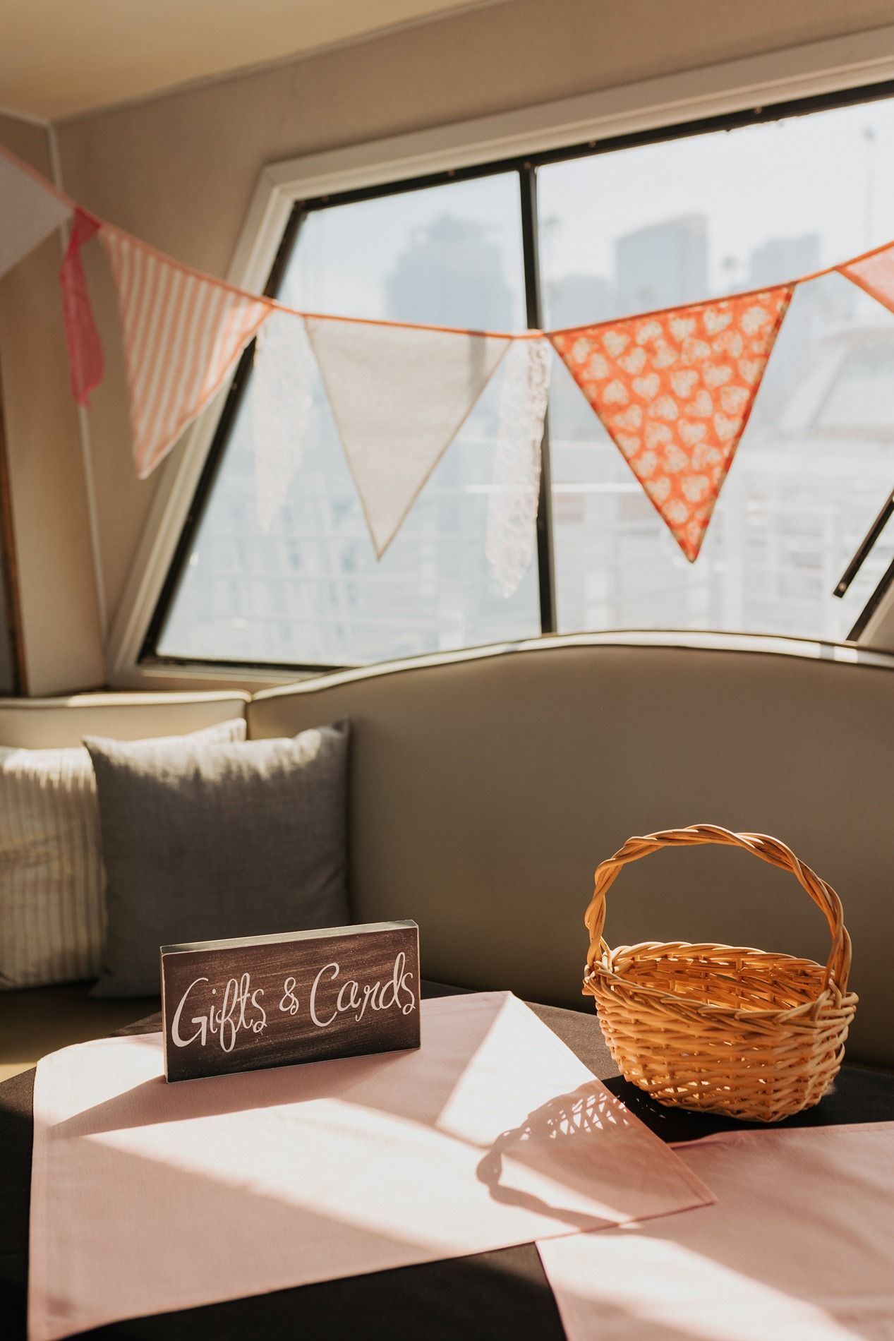 Pink and white bunting decorates a window ledge with rustic gift baskets and sign that says Gifts and Cards at a wedding reception.