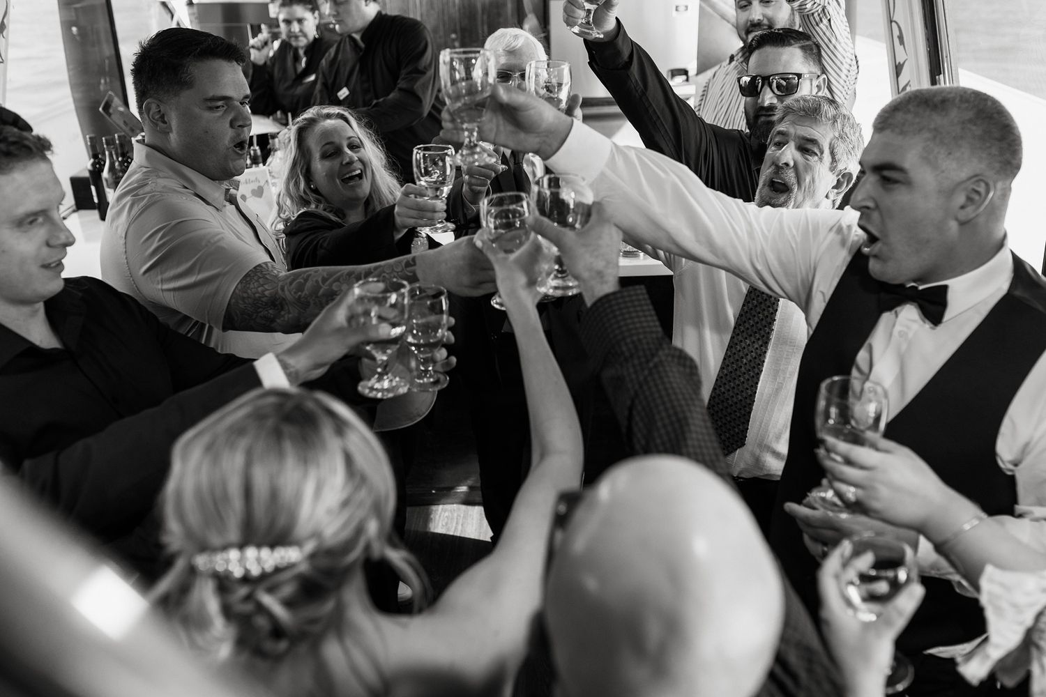 A black and white photo collage showing people raising glasses in celebration at a wedding reception on a boat in San Diego.