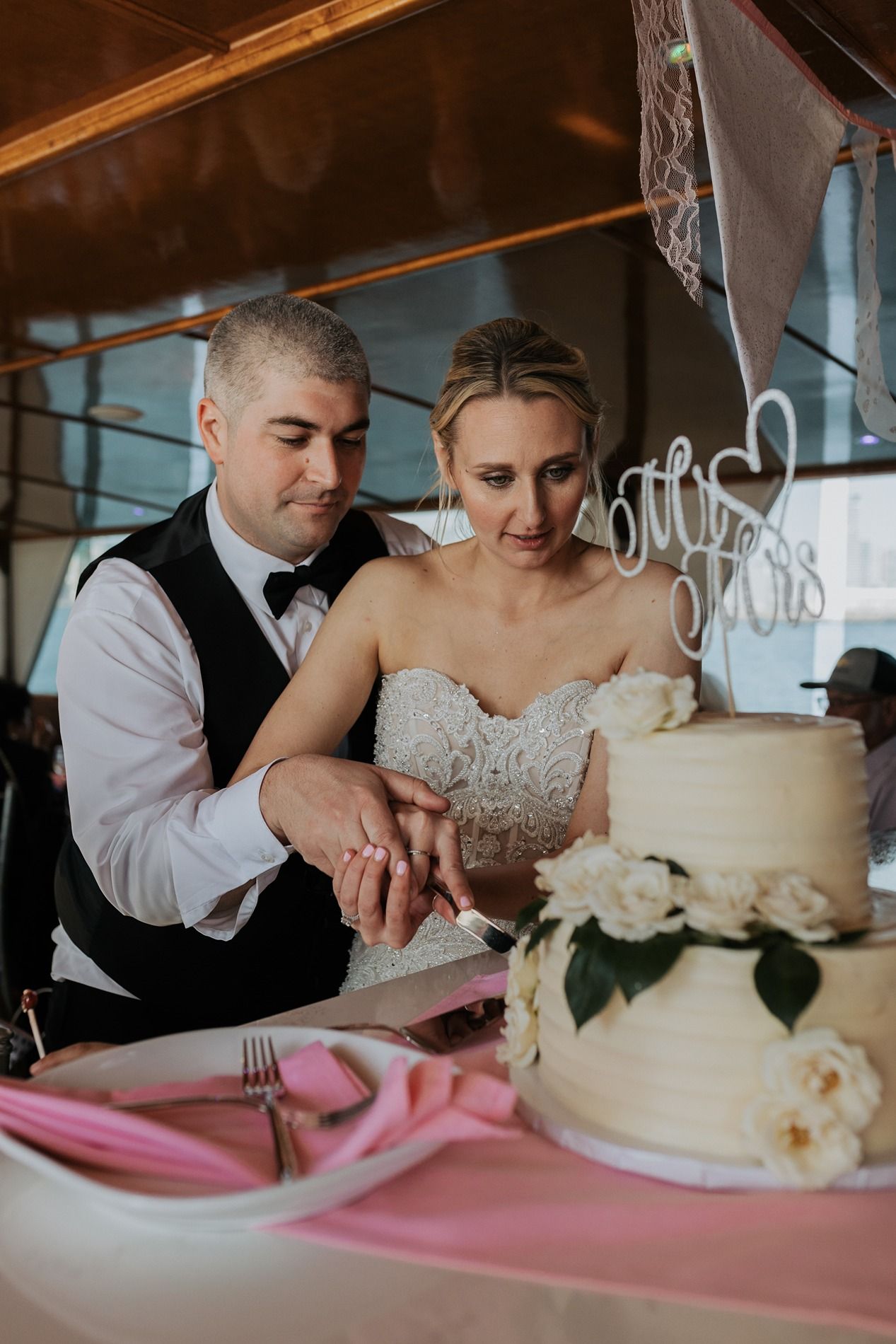 A couple cuts their wedding cake together with white floral decorations on a boat in San Diego.