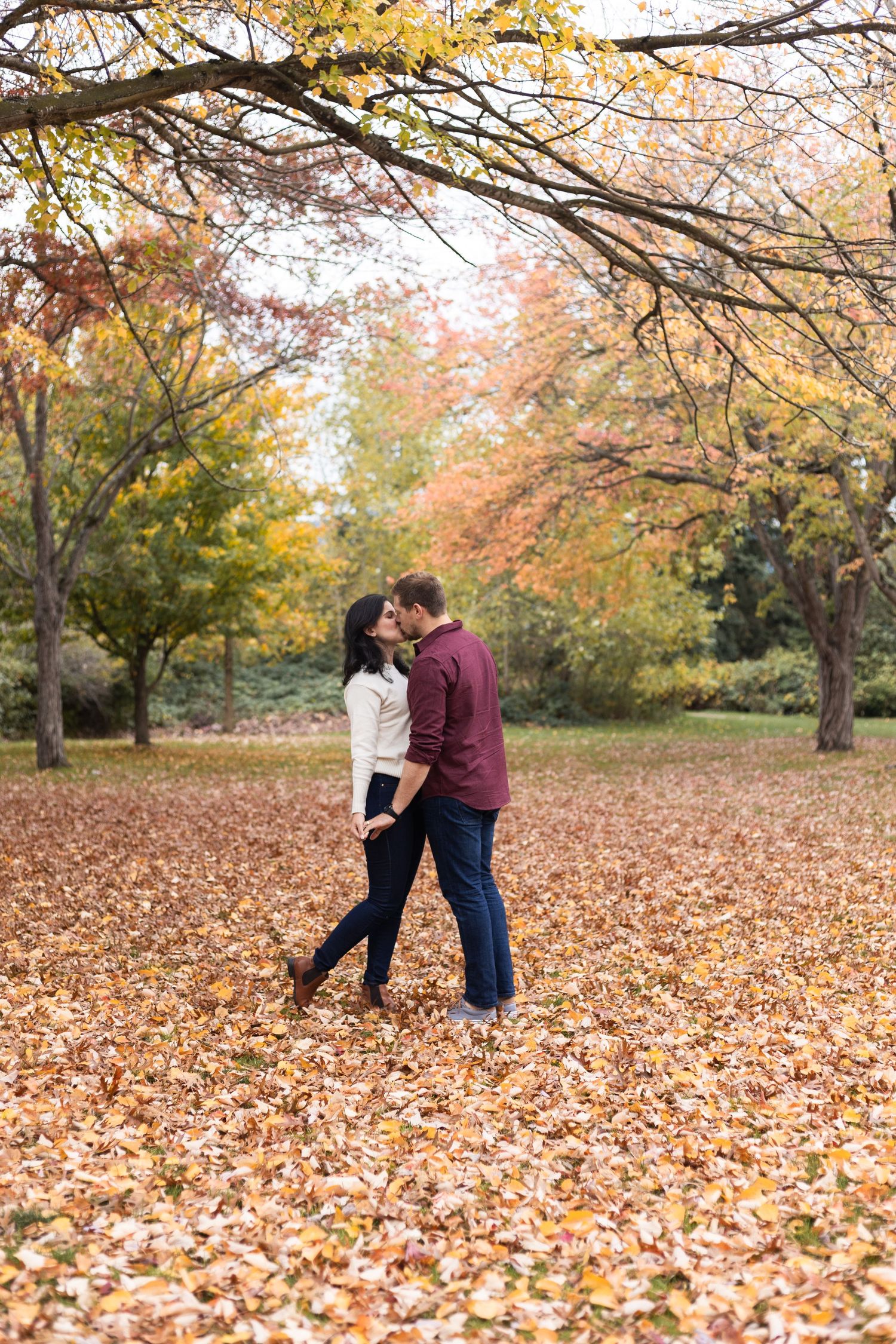 Couple dancing and embracing in a park covered with fallen autumn leaves.
