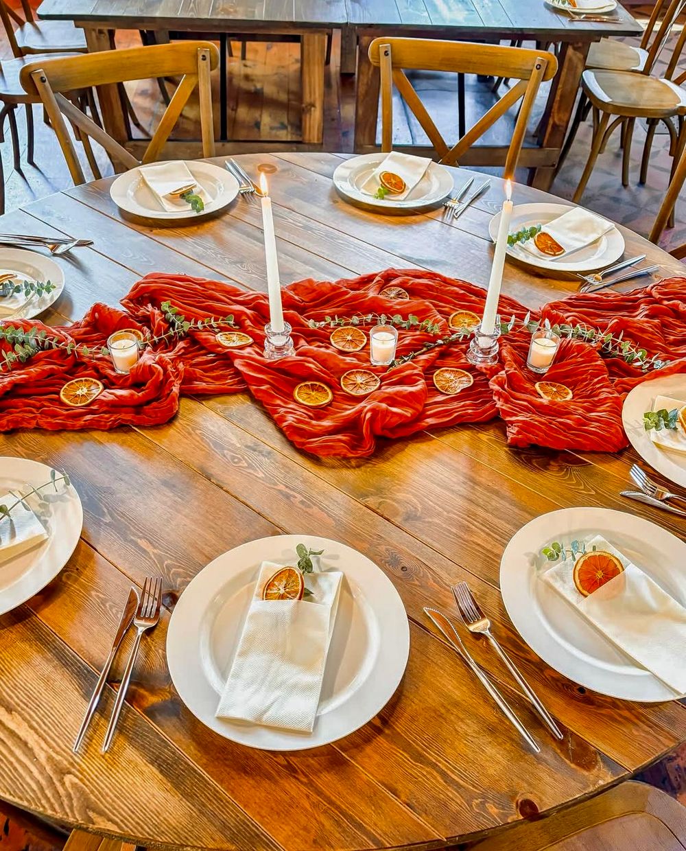 Rustic round wooden table set with red velvet runner, dried orange slices, and white candles.
