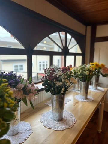 Silver buckets filled with colorful fresh flowers displayed on a wooden table by arched windows.