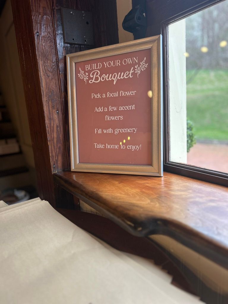 Framed sign on windowsill with Build Your Own Bouquet instructions for a DIY floral activity.