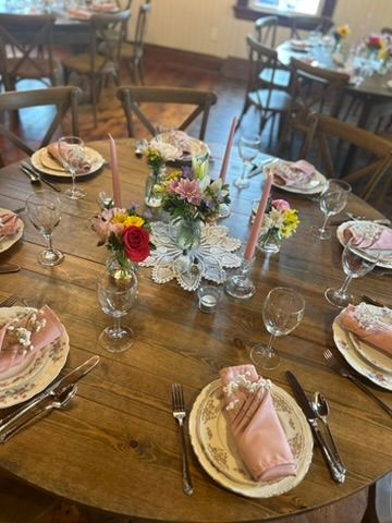 Round wooden table with pink napkins, vintage china, crystal glasses, pink candles, and colorful floral centerpieces.