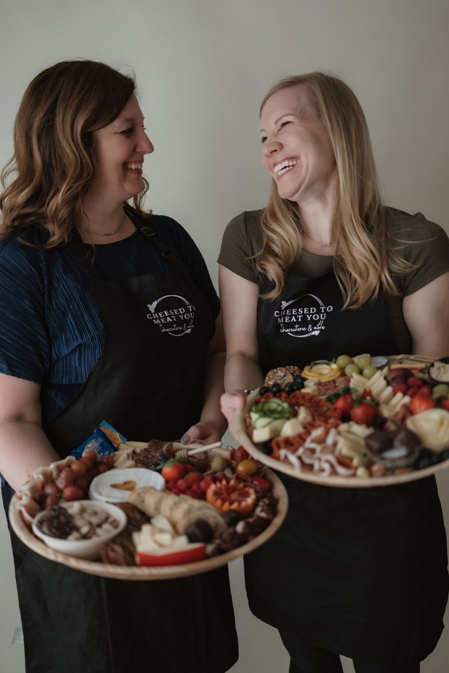 Two people sharing laughter and conversation while enjoying a charcuterie board with meats, cheeses and fruits.