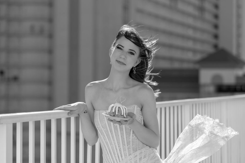 A bride in a white dress poses elegantly on a balcony railing with an ornate building in the background.