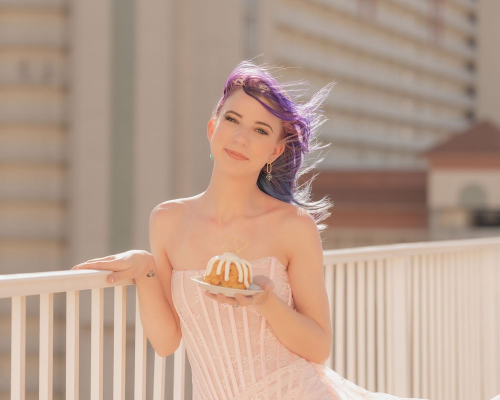 A person in a pink dress poses elegantly on a balcony with a dreamy sunlit atmosphere.