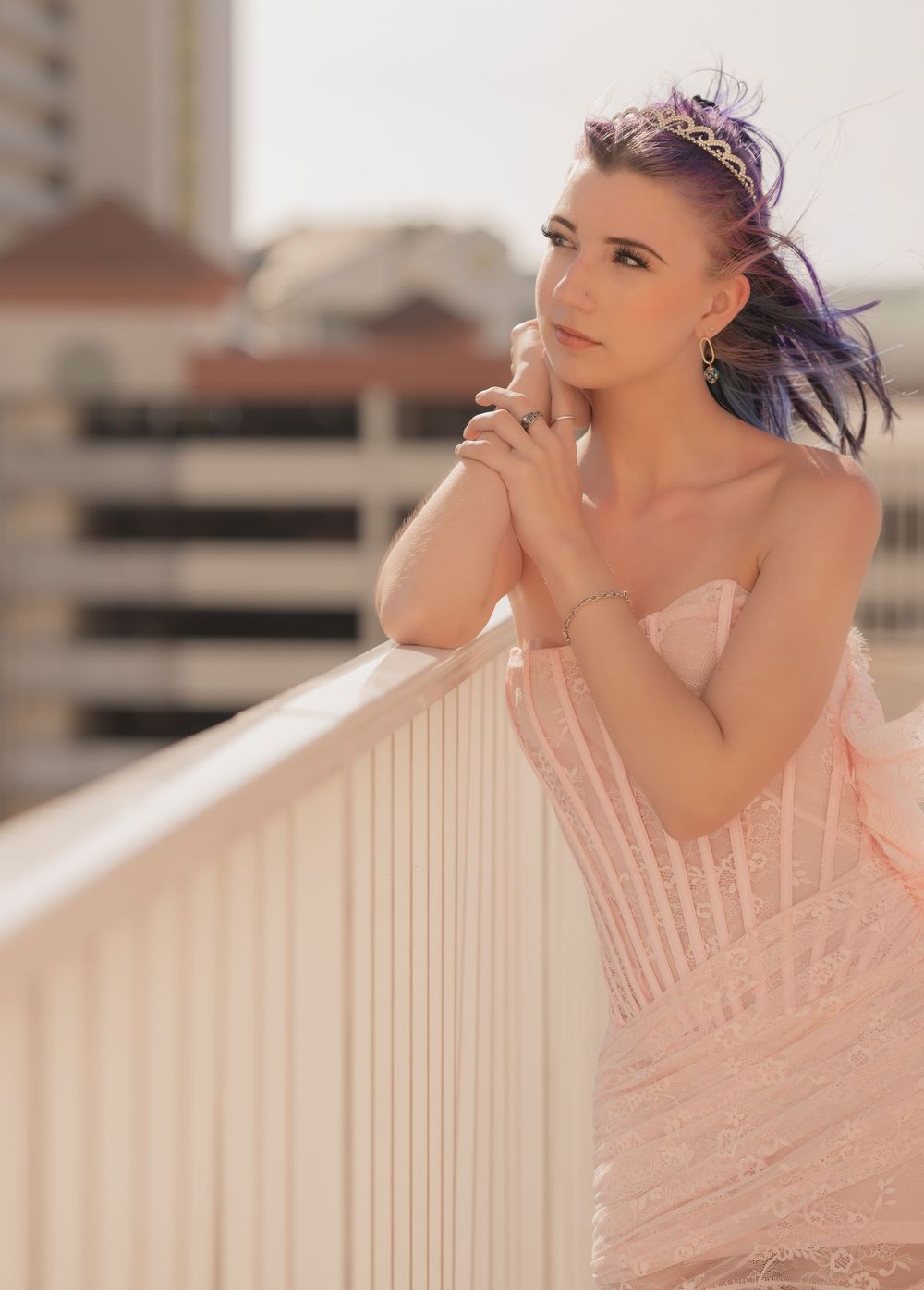 Woman in pink tulle dress poses gracefully against white railing in bright sunlit outdoor setting.