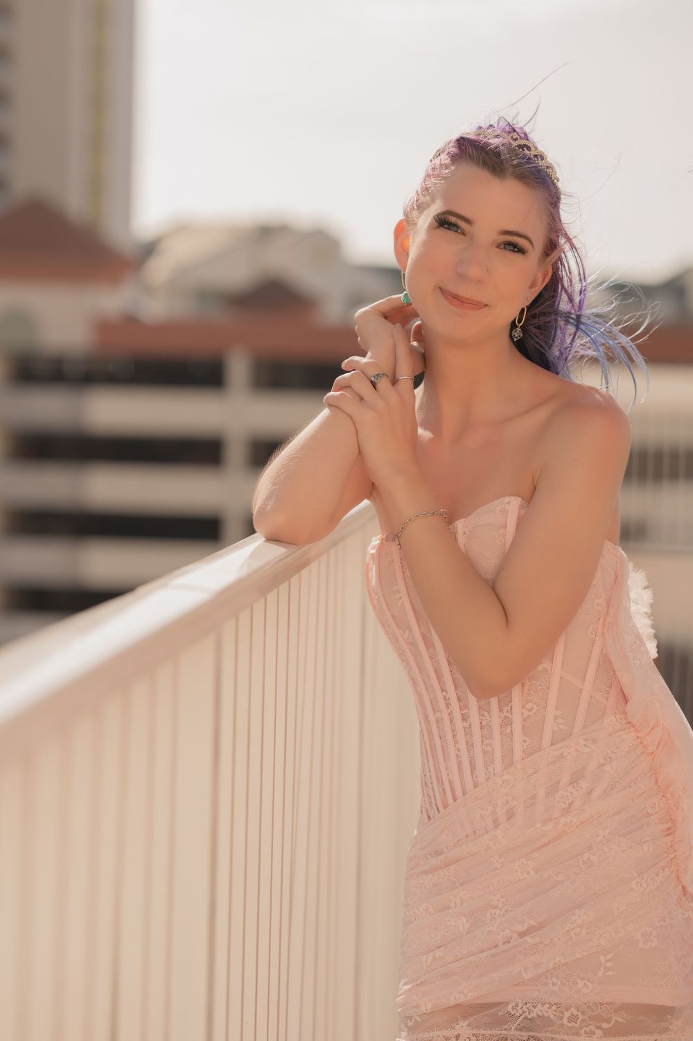 A person in a blush pink strapless gown poses elegantly against a white railing during golden hour.