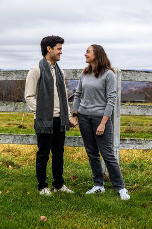 Casual couple photoshoot on grassy field with overcast sky background.