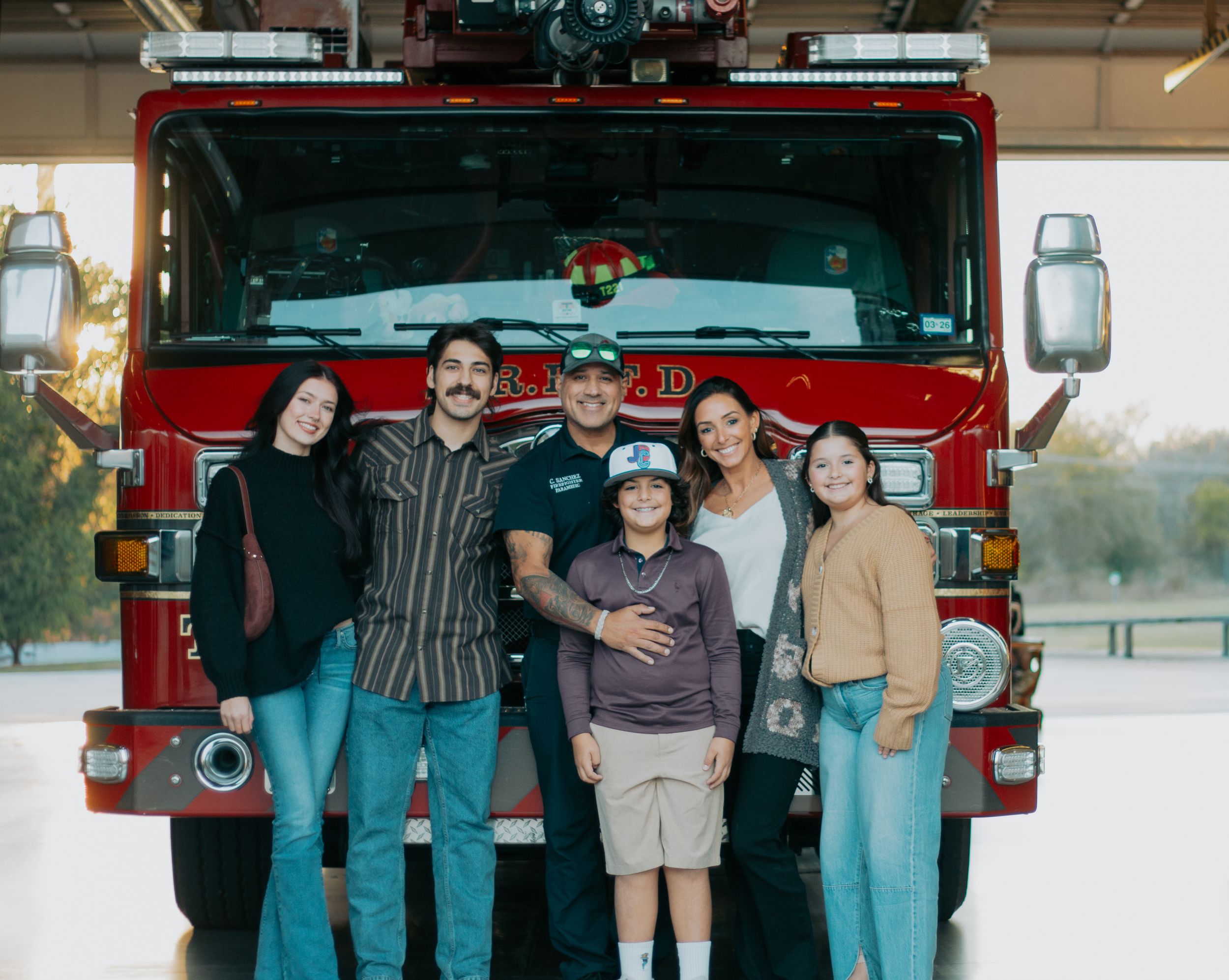 A group of mechanics in blue uniforms pose together in front of a red fire truck at a fire station.