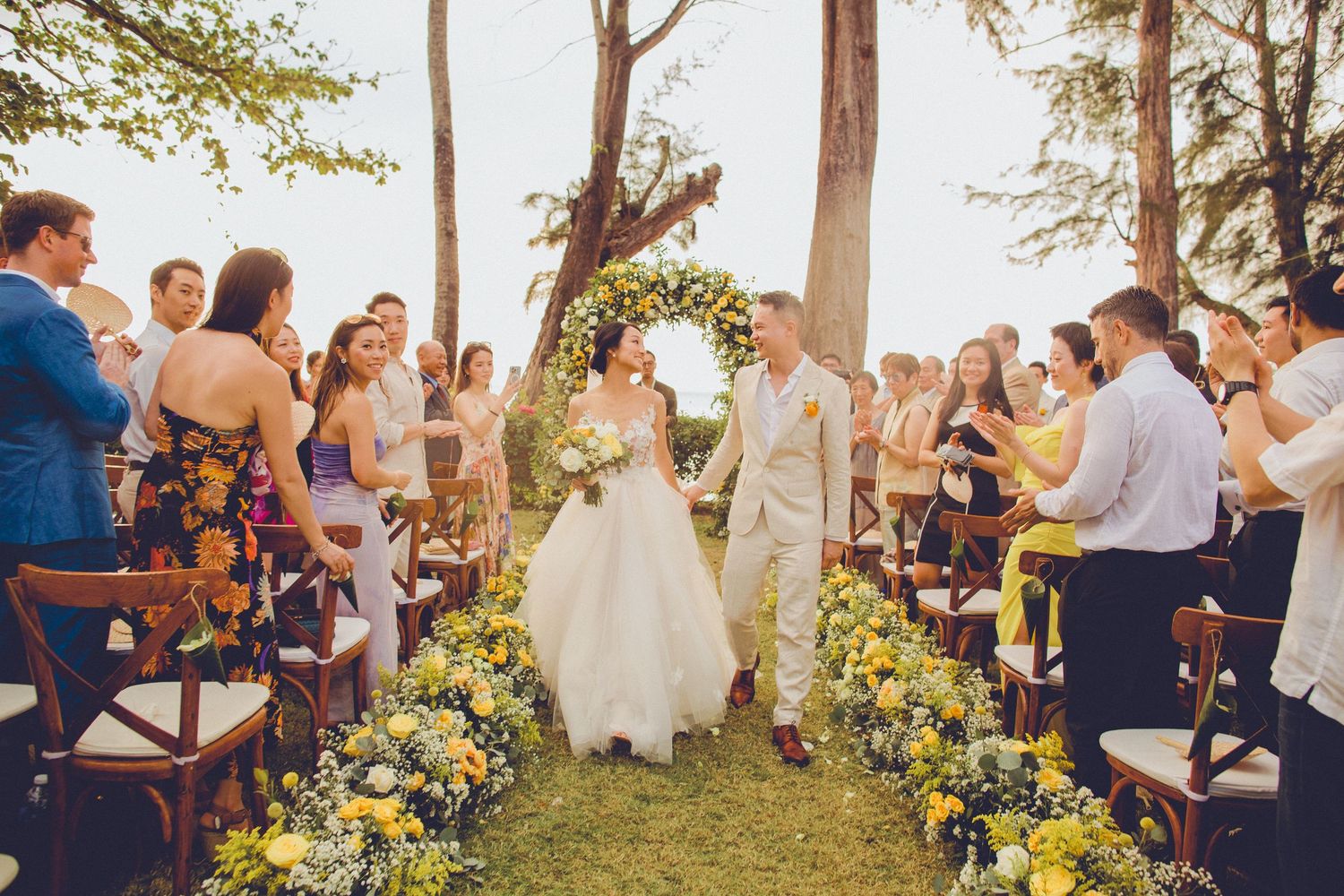 Bride and groom celebrate walking down the aisle at a Koh Samui outdoor wedding ceremony with floral arrangements and guest