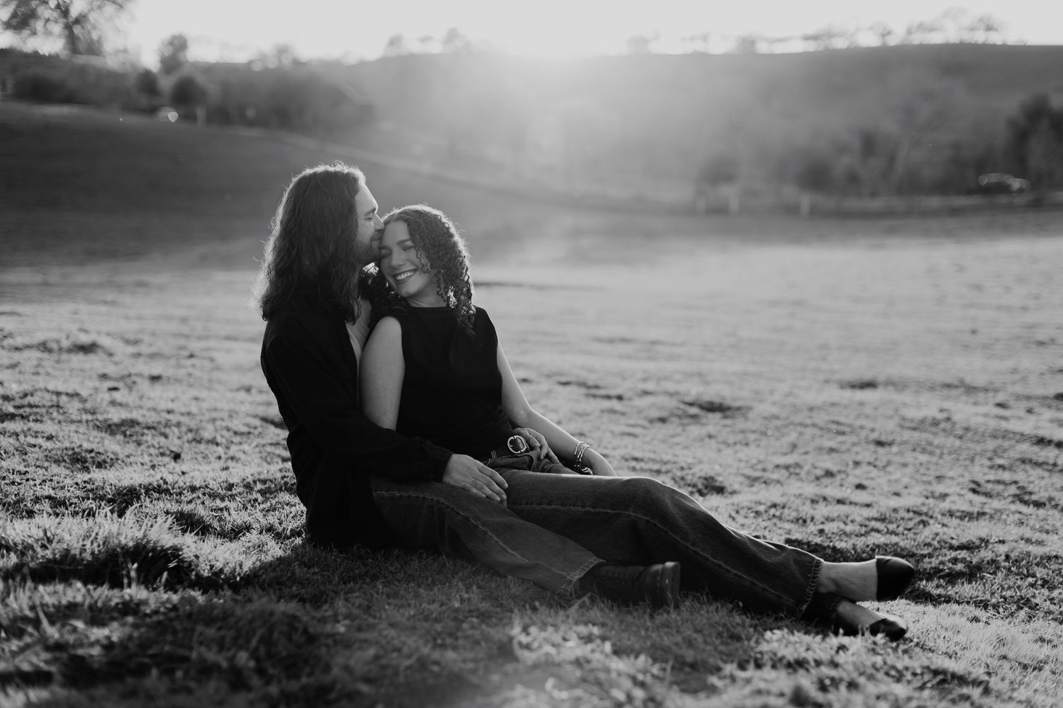 A silhouetted couple lies in a grassy field during a misty sunset creating a romantic atmospheric scene.